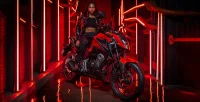 Perspectiva lateral direita da Moto Honda CB 300F Twister na cor Vermelho Com Mulher Na Moto Em Fundo Iluminado e Urbano 23