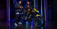 Vemos a Honda CB 300F Twister na cor Dourado Metálico Com Mulher E Homem Com Roupas Estilosas Fazendo Pose Ao Lado Da Moto Em Fundo Iluminado 21