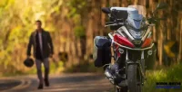 Frente da Moto NC 750X Vermelha em Estrada com Homem Segurando Capacete ao Fundo 26