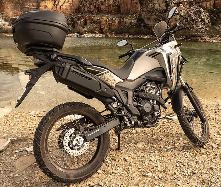Honda Sahara 300 Adventure: Trail off-road, bege metálico, top case, cenário rochoso